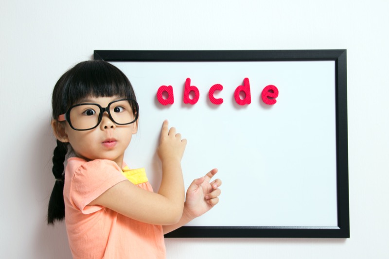La imagen muestra a una niña indicando unas letras en una pizarra