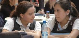 dos mujeres estudiantes conversan en una sala de clases
