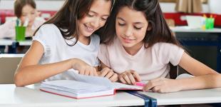 La imagen muestra 2 niñas revisando un cuaderno