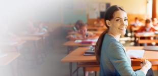 Fotografía de docente en sala de clases, sonriendo a la cámara.