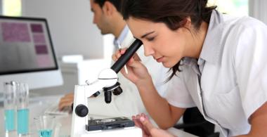 La imagen muestra a una mujer mirando por un microscopio