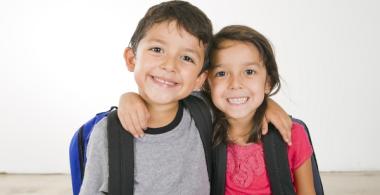 La imagen muestra un niño y una niña abrazados y sonrientes mientras posan para la fotografía