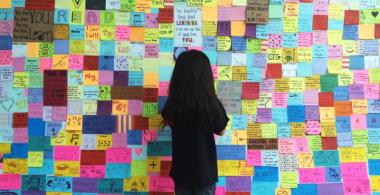 Imagen que muestra una pared repleta de post-it con ideas y una niña de espaldas mirando los pos it