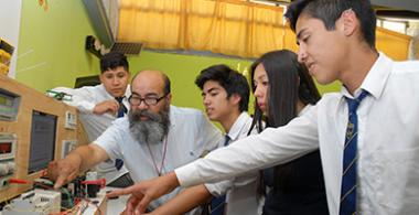 Profesor y sus estudiantes aprendienso sobre circuitos en liceo Técnico Profesional. 