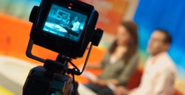Imagen que muestra una cámara de video grabando a dos locutores (hombre y mujer)