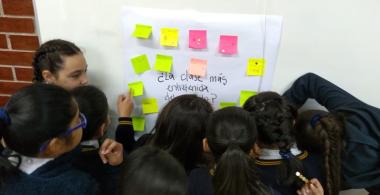 Estudiantes pegan en la pared ideas escritas en una papel