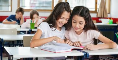Dos mujeres adolescentes comparten la lectura de un libro alegremente