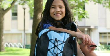 La imagen muestra a una niña con su mochila sentada en un parque