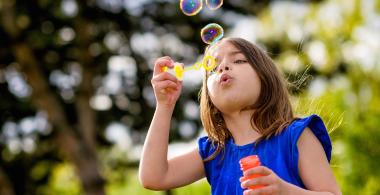 La imagen muestra una niña haciendo burbujas de jabón