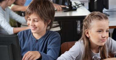 La imagen muestra a 2 estudiantes investigando en computadoras
