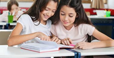 La imagen muestra 2 niñas revisando un cuaderno