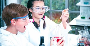 La imagen muestra a dos estudiantes en un laboratorio realizando experimentos con implementos científicos