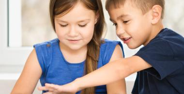 La imagen muestra a un niño y una niña observando algo en un dispositivo