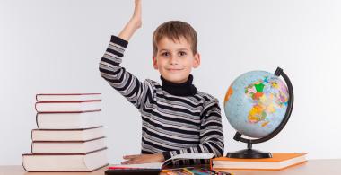 La imagen muestra a un niño con libros, lápices y globo terraqueo