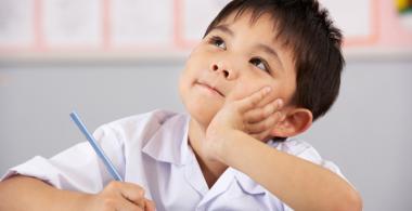 La imagen muestra a un niño con un texto y un lápiz en su mano mirando hacia arriba con gestos de pensamiento