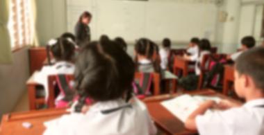 La imagen muestra una sala de clases con niños, niñas y una profesora