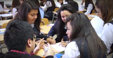 La imagen muestra un grupo de estudiantes conversando sobre un texto