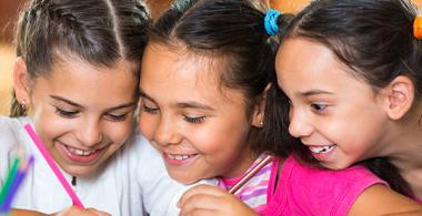 La imagen muestra 3 niñas mirando un texto o dibujo que realiza una de ellas