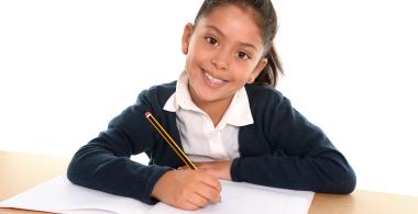 La imagen muestra a una niña sonriente escribiendo en un cuaderno