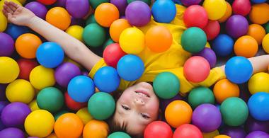 La imagen muestra a un niño sobre muchas pelotas de colores