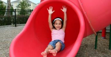 La imagen muestra a una niña en un resbalín en un parque
