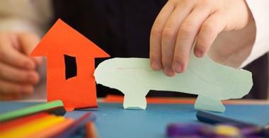 La imagen muestra la mano de un niño jugando con figuras de papel 