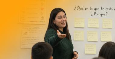 Fotografía de docente conversando con estudiantes en sala de clases.