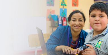 Fotografía de profesora estudiante varón mirando sonrientes hacia la cámara.